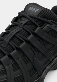 Μαύρο αθλητικό παπούτσι Nike με κοντινή άποψη της υφής του υφάσματος και των δερμάτινων λεπτομερειών, με περίπλοκο σύστημα κορδονιών και λογότυπο στη γλώσσα.