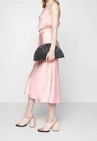 Vaaleanpunainen satiinimekko, jossa on su losse tiivistys, yhdistettynä vaaleisiin avonaisiin nilkkureihin ja mustaan, fanimuotoiseen clutch-laukkuun. Sujuva pinta, moderni muotoilu.