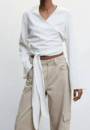 Kvinde iført en hvid, stribet slå-om-bluse bundet i taljen med lange ærmer og beige cargobukser med lommer.