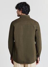 Camicia a maniche lunghe di colore verde oliva, realizzata in tessuto liscio, con un taglio dritto, yoke posteriore e spacchi laterali all'orlo per un maggiore movimento.