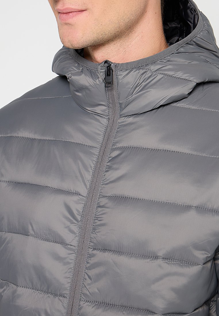 Chaqueta de plumas gris con un alto cuello, cierre delantero con cremallera y un diseño acolchado ligero. Presenta una textura suave y un brillo sutil.