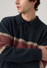 Knitted pullover in dark blue wool with a collared neck. Features horizontal stripes in beige and red, and button details on the front.