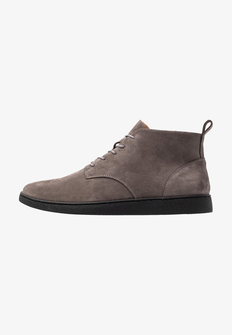 Bottes chukka en daim gris avec semelles en caoutchouc noir, dotées d'une fermeture à lacets, d'une languette à l'arrière et d'une texture lisse.