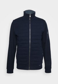 Chaqueta azul marino con cierre frontal, cuerpo acolchado, mangas de canalé y cuello alzado. Cuenta con un bolsillo con cremallera en el brazo y un acento de logo.