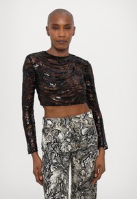 Fekete, flitteres, hosszú ujjú crop top, texturált mintával és kerek nyakkivágással, mintás, magas derekú kígyómintás nadrággal párosítva.