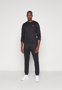 Svart sweatshirt och byxor i mjukt tyg, med ribbade muddar och en diskret logotyp på bröstet, tillsammans med vita sneakers.