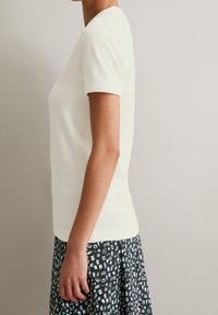 Krämfärgad kortärmad T-shirt i ribbad textur, matchad med en mönstrad svart och ljusblå kjol med abstrakta former och mönster.