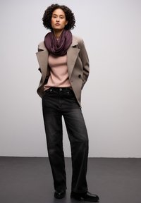 Manteau gris croisé porté sur un pull rose, associé à un jean noir à jambes larges et des bottes noires. Une écharpe violet foncé est drapée autour du cou.