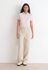 Camisa polo rosa clara com colarinho, combinada com calças bege de cintura alta e ténis brancos de plataforma. Design simples e de corte reto.