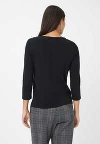 Zwart 3/4 mouwen top met een ronde halslijn, een zachte textuur en een rechte zoom. Gecombineerd met grijs geruite broek met een ruitpatroon.