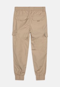 Beige cargobroek met elastische tailleband, taps toelopende boorden en meerdere opgestikte zakken op de achterkant en zijkanten. Gladde, lichte stof.
