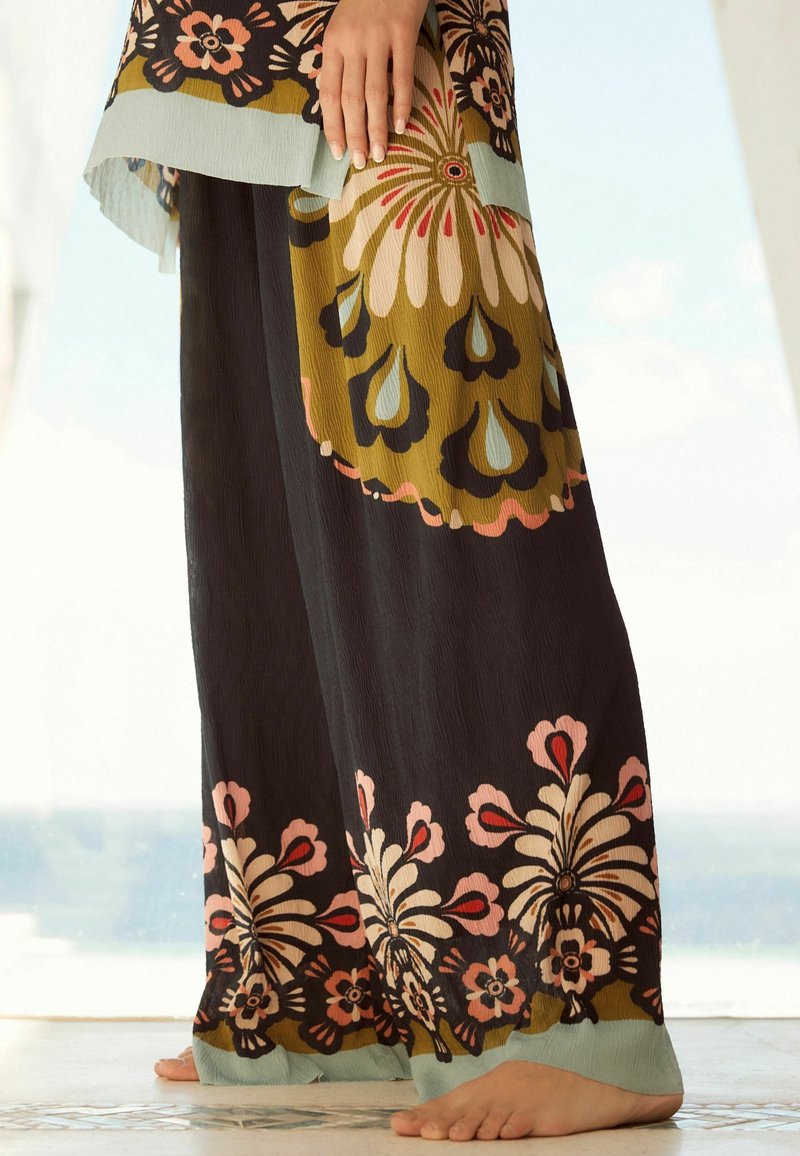 Pantalon fluide à motifs en tissu léger. Présente des motifs floraux audacieux en noir, olive, rose et aqua. Coupe décontractée et texture.
