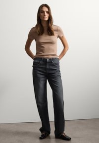 Camiseta beige de canalé, jeans de mezclilla oscuros de corte holgado, zapatos negros, fondo neutro. Look casual con texturas y colores distintos.