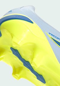 Gros plan sur la semelle d'une chaussure de football jaune néon et grise avec des crampons moulés et une barre de soutien "POWERFRAME".