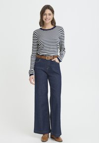 Chemise à manches longues rayée bleu marine et crème, associée à un pantalon en denim taille haute à jambes larges. Ceinture en cuir marron et chaussures marron complètent le look.