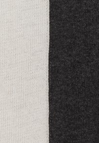 Tissu tricoté avec de larges rayures crème et gris anthracite. La texture est douce et légèrement duveteuse, avec un motif de points uniforme.