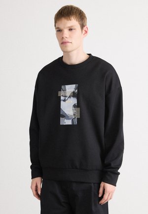 Zwarte sweatshirt met een ronde hals, voorzien van een centraal grafisch paneel met abstract ontwerp en gouden accenten. Gemaakt van zachte stof.