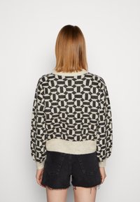 Maglione lavorato a maglia con un motivo geometrico in bianco e nero, polsini e orlo a coste, abbinato a pantaloni corti in denim scuro.