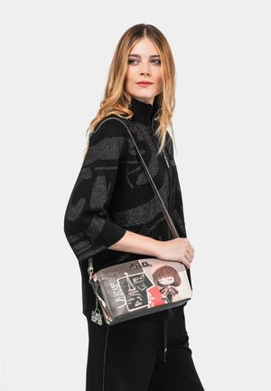 Bolso cruzado con una tela gris suave que presenta gráficos de dibujos animados y acentos de texto. Incluye herrajes de plata y una correa ajustable.