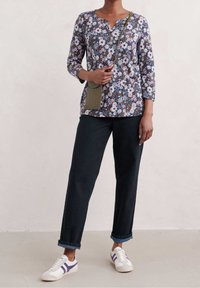 Blommig långärmad topp med djup halsringning, kombinerad med lösa mörka jeans och vita sneakers med lila detaljer. Avslappnad, texturerad tyg.