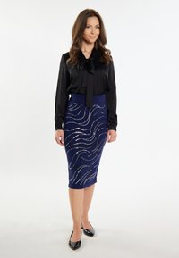 Blusa nera con dettaglio a fiocco, abbinata a una gonna lavorata a maglia blu navy lunghezza ginocchio con motivi a onde argentate. Ballerine nere a punta.