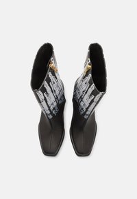 Botines de cuero negro hasta el tobillo con puntera afilada, que cuentan con un cierre de cremallera y un diseño gráfico decorativo en gris y blanco en el cañón.