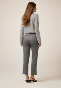 Szary sweter z dekoracyjnym wzorem w romby, szare dopasowane spodnie oraz czarne sandały na obcasie, prezentujące dopasowaną sylwetkę i miękką teksturę.