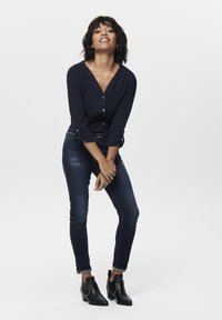 Camicia blu navy con bottoni, maniche lunghe, abbinata a jeans skinny scuri e stivaletti neri alla caviglia con dettagli in borchie. Look semplice e moderno.