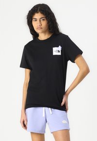 Črna majica s kratkimi rokavi, ki ima belo kvadratno nalogo in vijolično cvetlico na levem prsnem delu. Prijeten kroj.