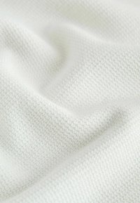 Gros plan d'un tissu tricoté blanc et doux montrant un motif texturé et des plis légers.