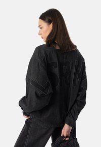 Czarna, oversize'owa kurtka dżinsowa z dużym haftowanym logo "SRM" na plecach, z opuszczonymi ramionami i teksturowanym wykończeniem.