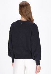 Marineblauwe gebreide trui met een ontspannen pasvorm, cropped lengte en ballonsleeves, met geribbeld textuur en knoopaccenten bij de manchetten.