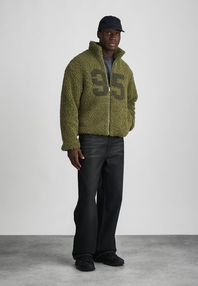 Olive green, zippered fleece jacket with a plush texture and large black "35" print on the front. Paired with black wide-leg pants and sneakers.