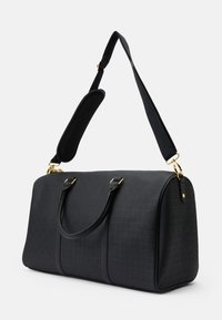 Mala de viagem preta feita de material texturizado com detalhes em dourado, alças duplas e uma alça de ombro ajustável e acolchoada.