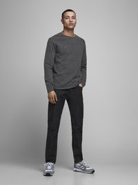 Grå langermet skjorte, mørke jeans og grå joggesko. Uformell stil, ensfarget tekstur uten mønstre. Modell som står mot en ensfarget bakgrunn.