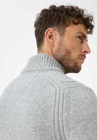 Grauer Strickpullover mit Rippkragen, der strukturierte Muster an den Schultern und eine taillierte Passform aufweist. Weiches Wollmaterial sichtbar.