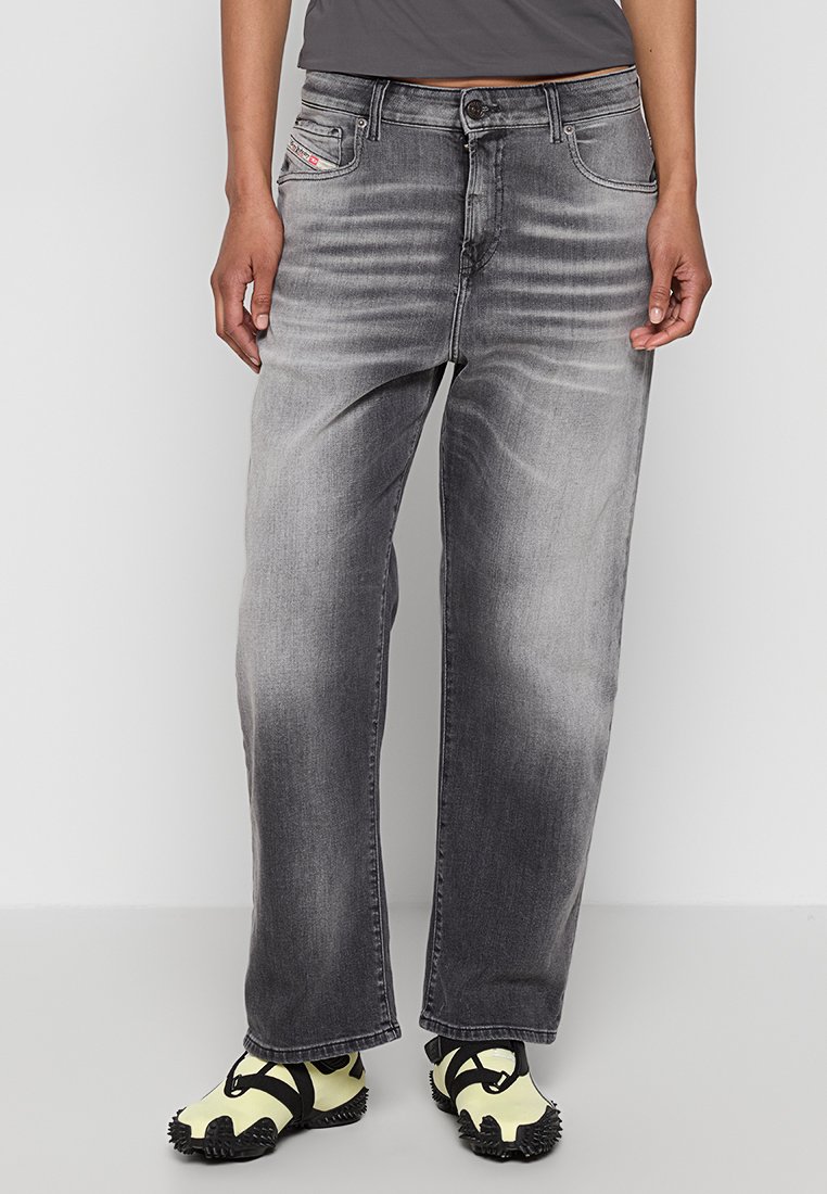 Jeans in denim grigio con una vestibilità rilassata, con aree sbiadite e tasche frontali. Abbinati a scarpe sportive nere e gialle.
