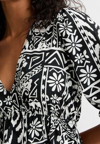 Abito a righe in bianco e nero con motivi floreali e geometrici, scollatura a V, maniche a palloncino e vita elastica per una vestibilità comoda.