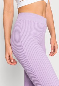Leggings lilás canelados com uma cintura alta. O tecido é macio, apresentando riscas verticais para textura e detalhes subtis ao longo das costuras.