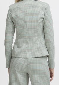 Světle modrý kostkovaný sako a odpovídající kalhoty, s fitted designem a jemnou texturou, doplněné hnědými akcenty v mřížkovaném vzoru.