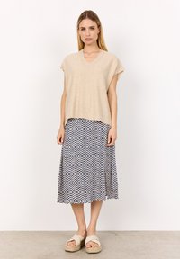 Beige stickad topp med V-ringning och korta ärmar, kombinerad med en midikjol i marinblått och vitt med zigzag-mönster. Bärs med beige plattformssandaler.