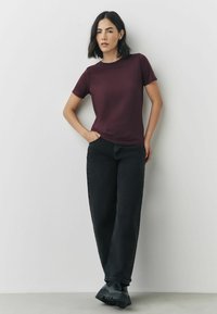 Bordeaux-farvet tætsiddende t-shirt lavet af blødt stof, parret med højtaljede sorte jeans med en afslappet pasform og brede ben. Sorte chunky støvler.