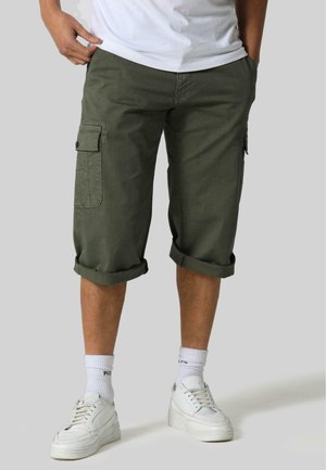 Olive green cargo shorts made of cotton with rolled hems, featuring side pockets and a relaxed fit, paired with white sneakers and socks.