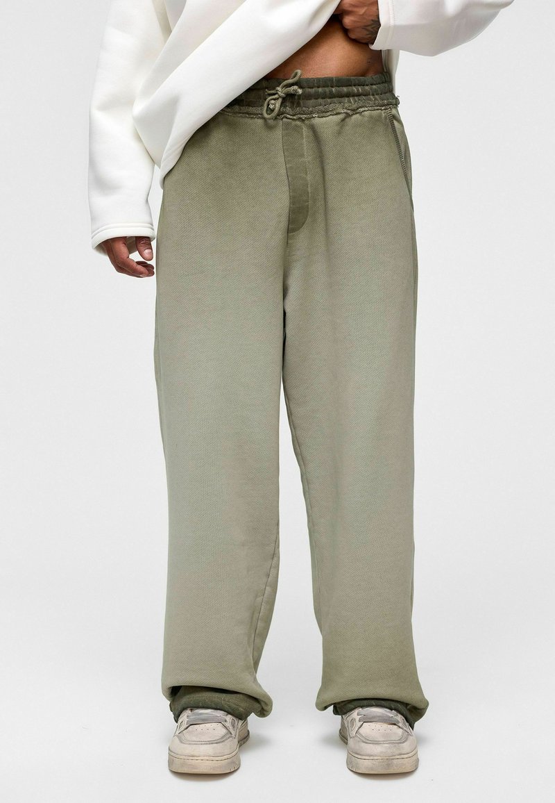 Licht olijfgroene sweatpants met een trekkoord in de taille, taps toelopende boorden en een textuurstof, gecombineerd met witte sneakers.