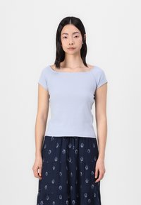 Top azul claro, de mangas curtas e com textura canelada, com decote quadrado, combinado com uma saia azul-marinho com padrão de folhas. Textura suave, design ajustado.