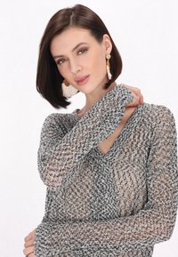 Gestrickter Pullover in Schwarz und Weiß, mit einem V-Ausschnitt und langen Ärmeln in einem lockeren, strukturierten Design. Akzente setzen große Ohrringe.