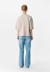 Lys beige oversized top med korte ærmer, parret med lys blå flagrende jeans. Blød tekstur med minimal sømdetaljering på skuldrene.