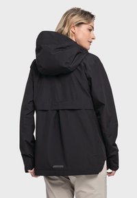 Schwarze wasserdichte Jacke mit Kapuze, lockerer Schnitt, elastischen Bündchen und einem lichtreflektierenden Detail auf der Rückseite. Glatte Textur.