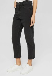 Vaqueros negros de cintura alta con corte recto, que cuentan con bolsillos delanteros, cremallera y dobladillo sin rematar. Combinados con zapatillas blancas.