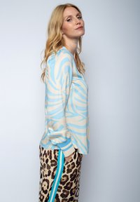 Lichtblauwe en crèmekleurige blouse met patroon en lange mouwen, gecombineerd met leopardprint broeken met een blauwe streep aan de zijkant.